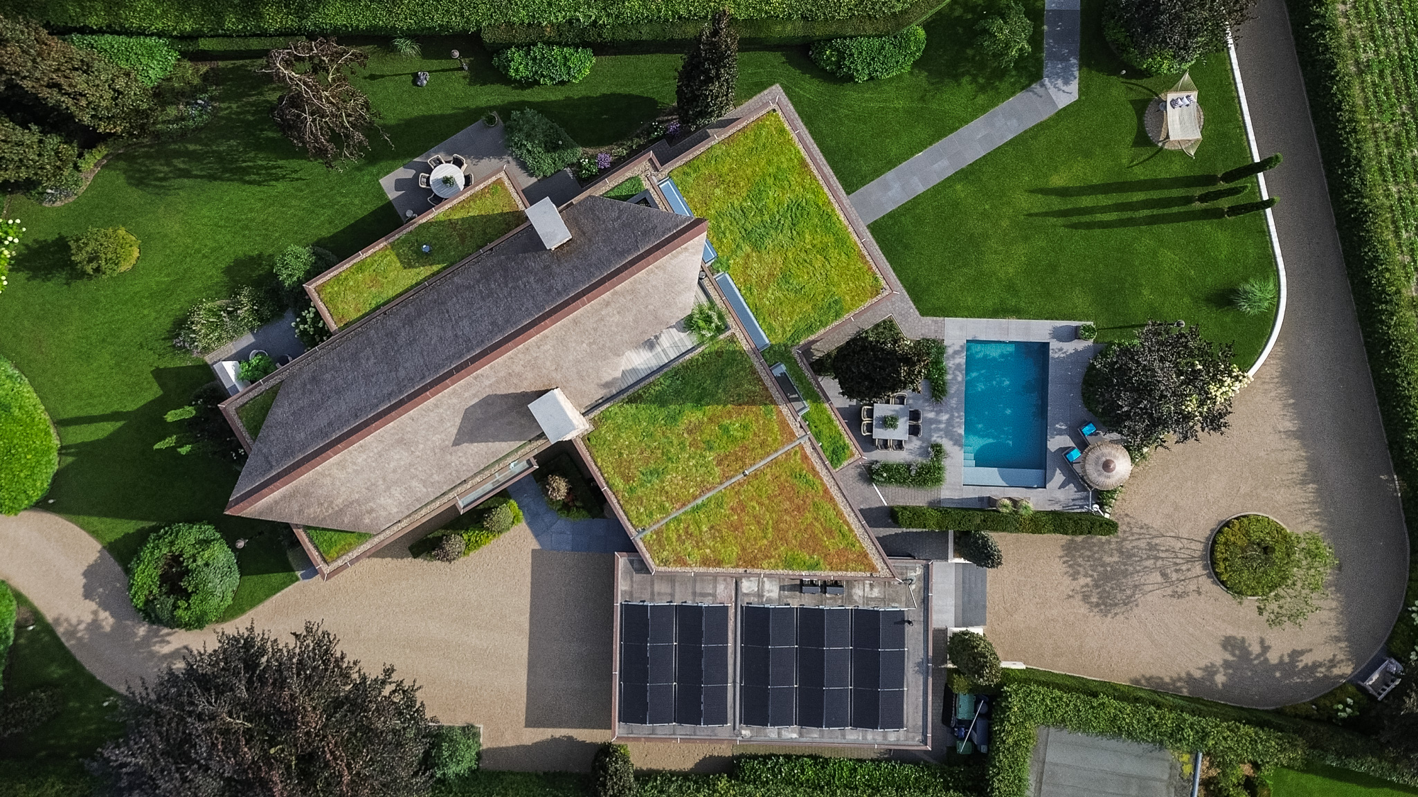 Luchtbeeld van een woning met groene daken, oprijlaan en zwembad